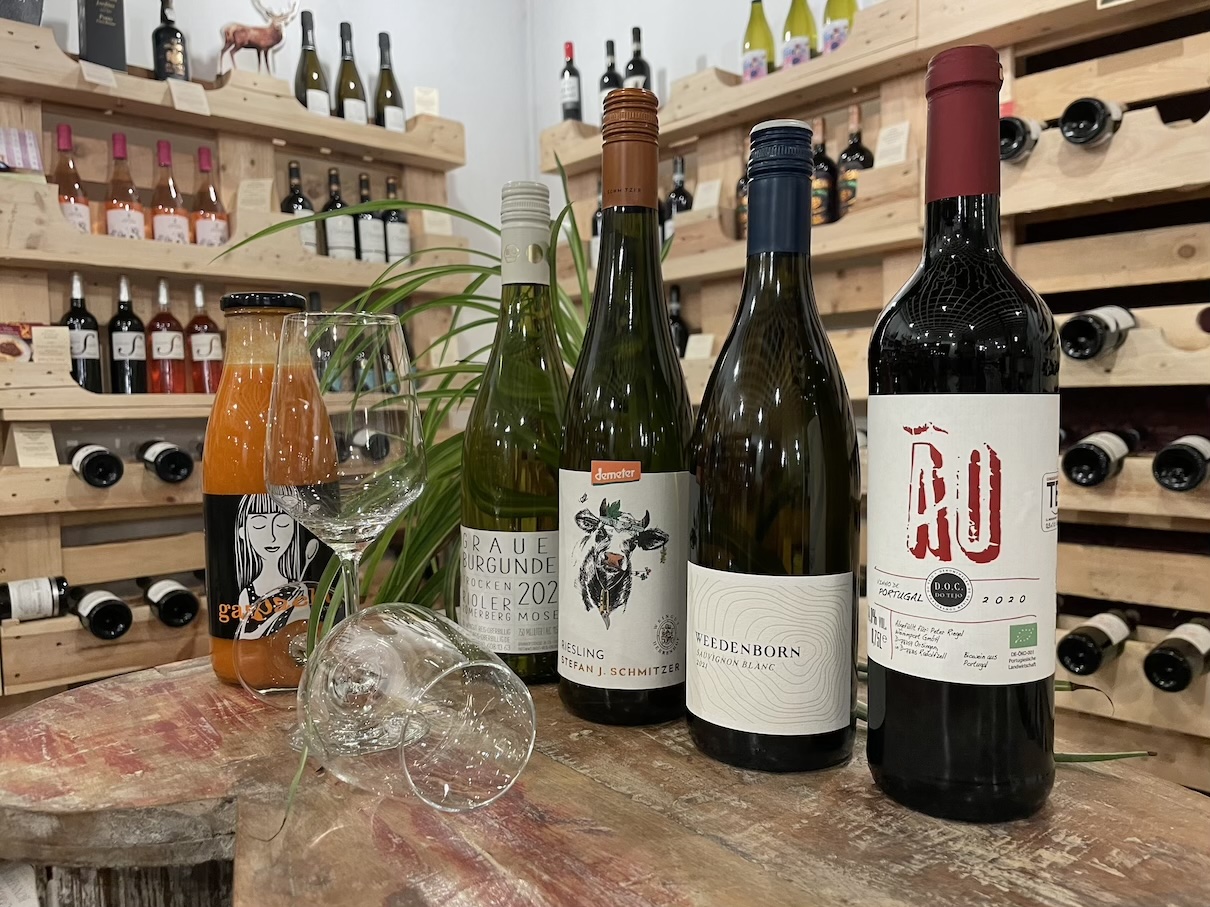 Auf einer rustikalen Holzplatte stehen mehrer Weinflaschen, ein Karottensaft und zwei Weingläser.