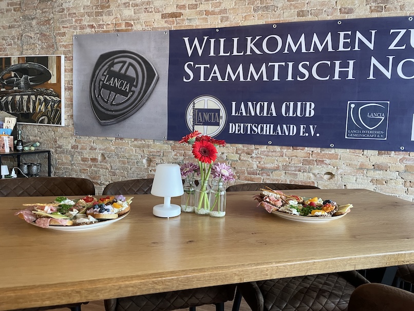 Ein Tisch mit zwei Tellern mit Häppchen. Dahinter ein Banner des Lancia Clubs.