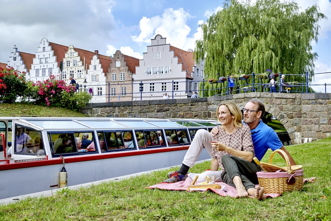 Ein Paar macht ein Picknick mit Wein am Fluss und eine Gracht fährt vorbei.